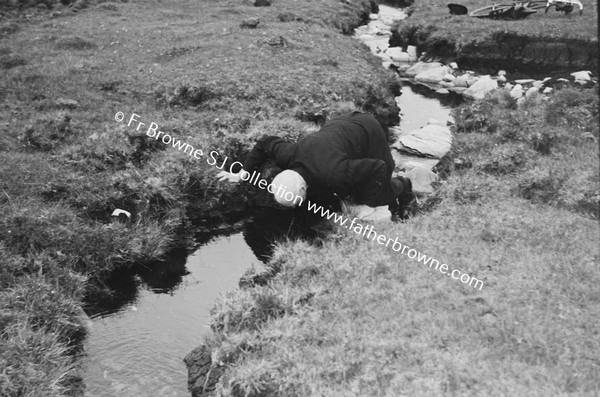 MAN CROSSING STREAM CARRYING BICYCLE